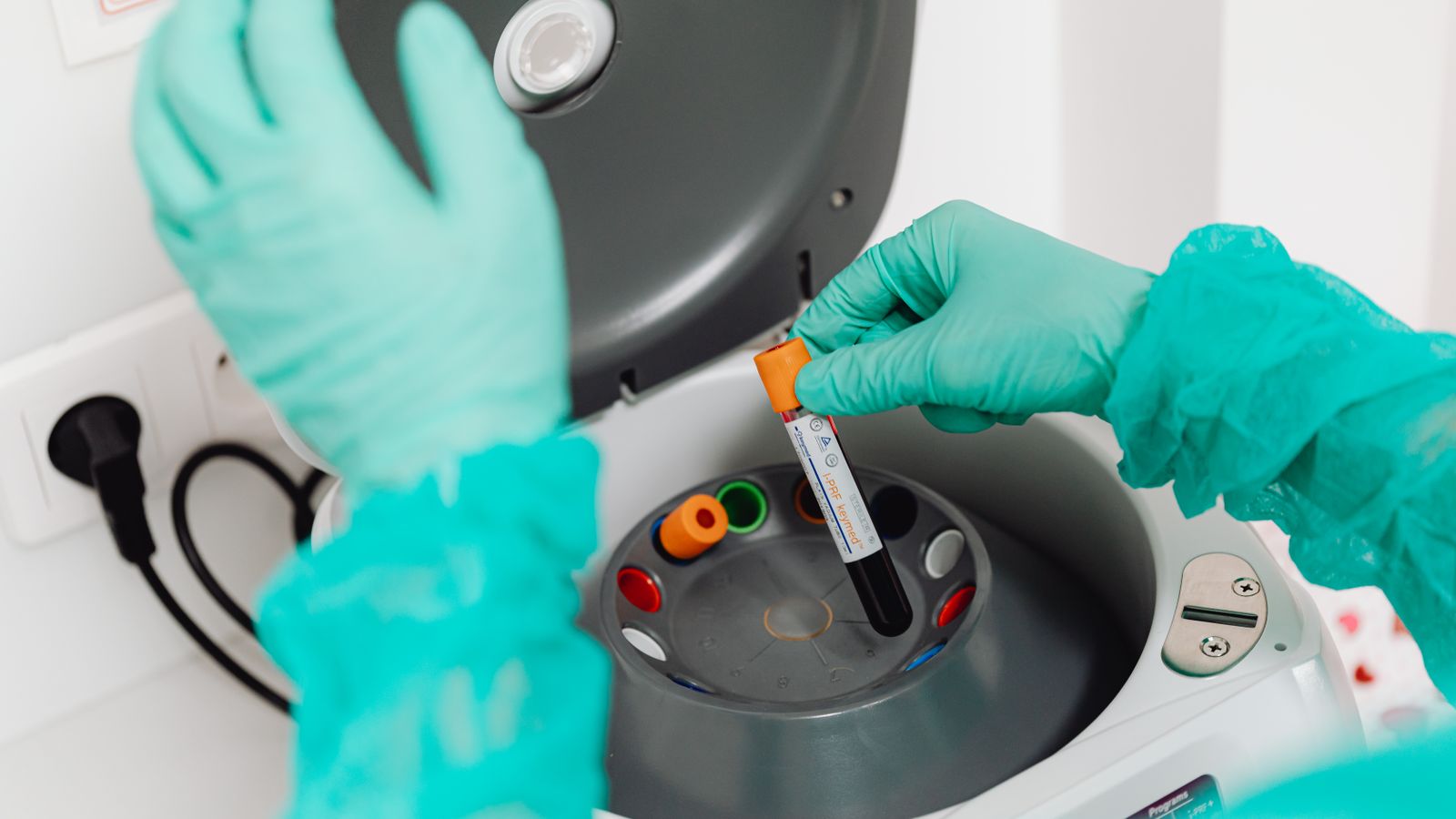 A gloved lab technician operates a centrifuge during blood analysis in a modern laboratory.