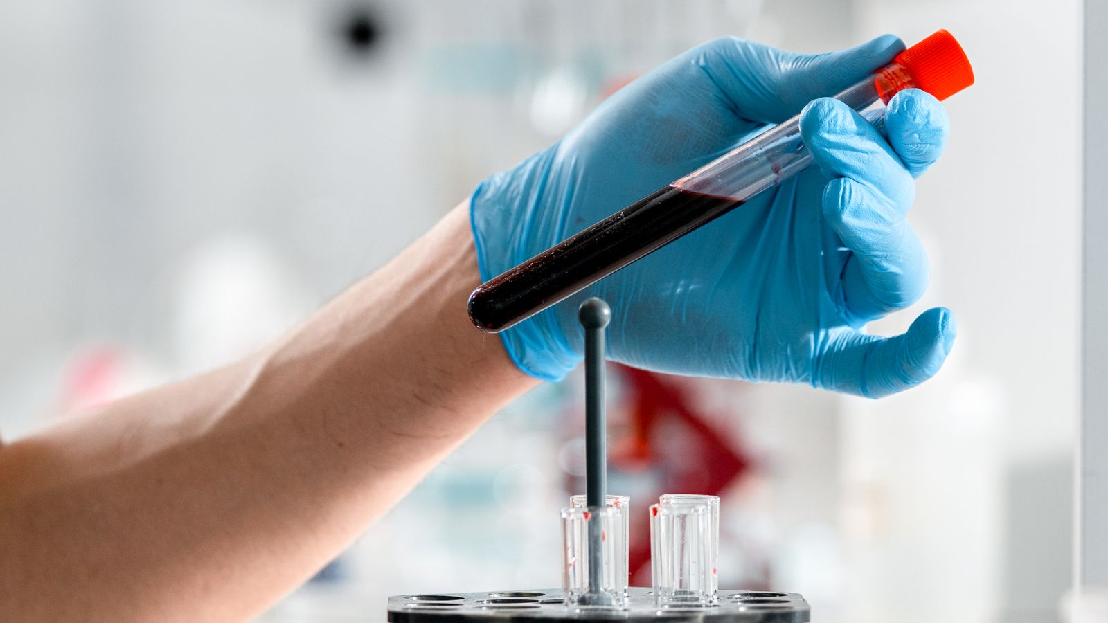 A gloved hand holding a test tube containing a blood sample in a clinical research laboratory.