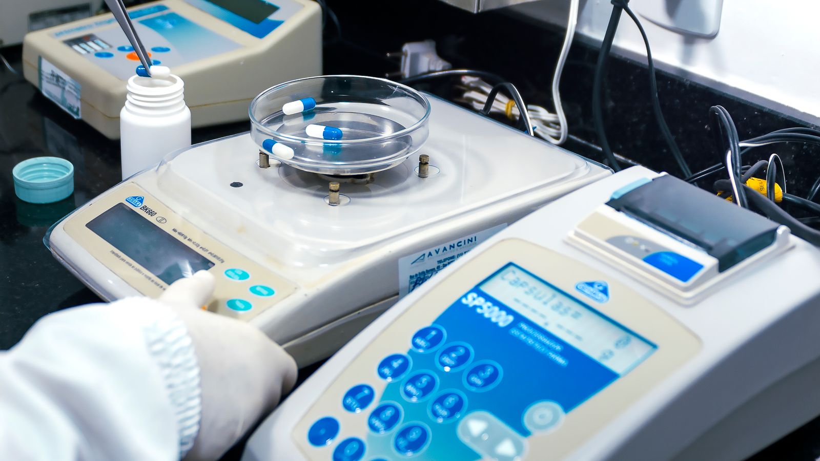Close-up of laboratory equipment on a bench beside a small cluster of capsules, arranged for pharmaceutical analysis.